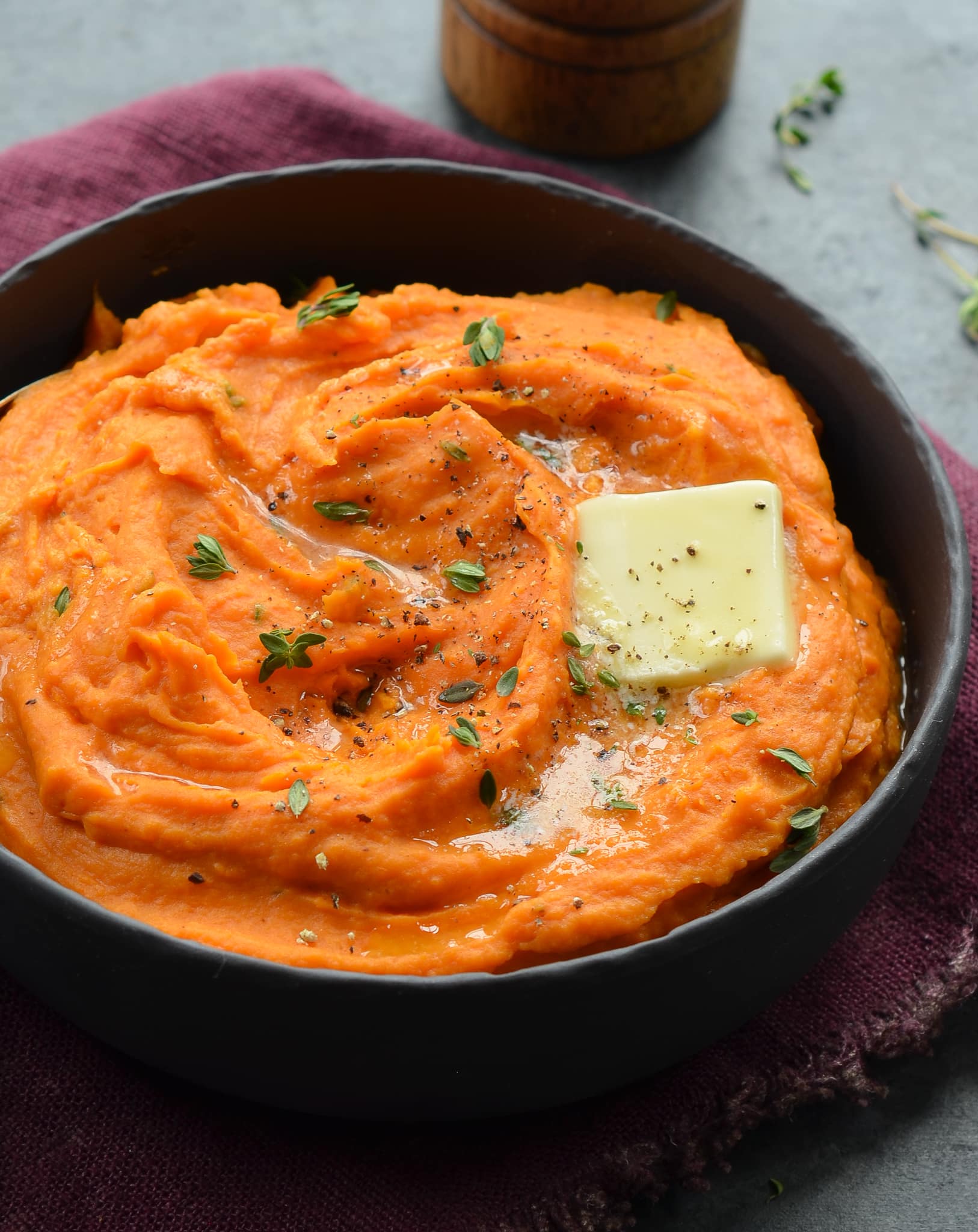Mashed sweet potatoes in a black bowl topped with butter.