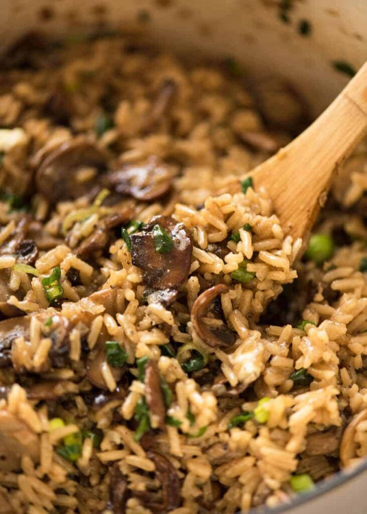 Mushroom rice in a large pan with a wooden spoon.