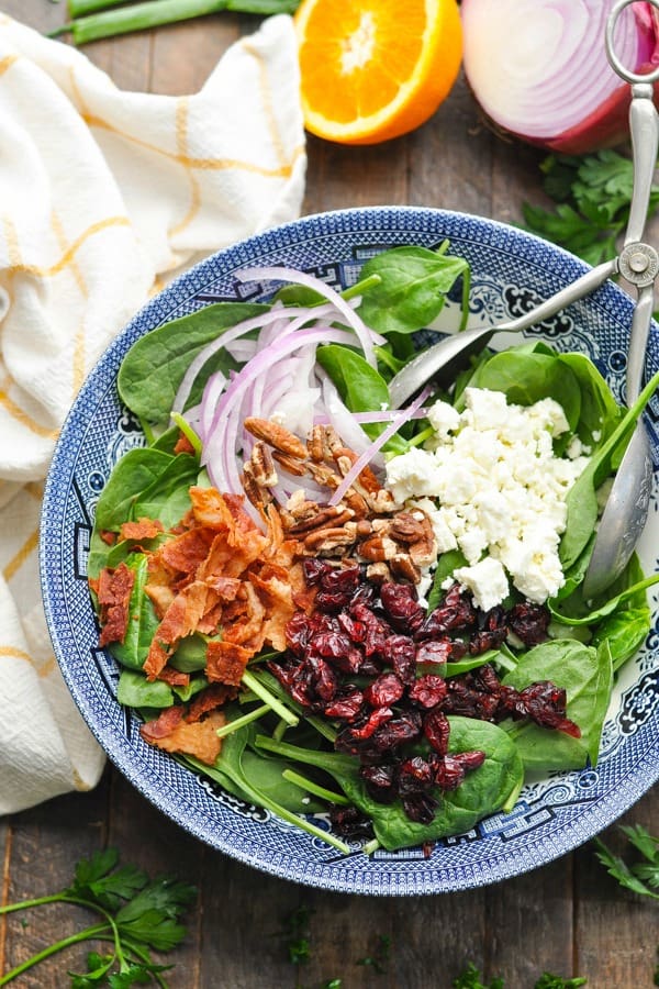 Mixed winter salad with spinach, bacon and cranberries in a blue bowl. 