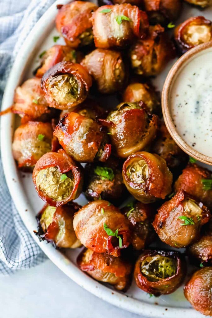 Bacon wrapped brussels sprouts on a plate with a white sauce.