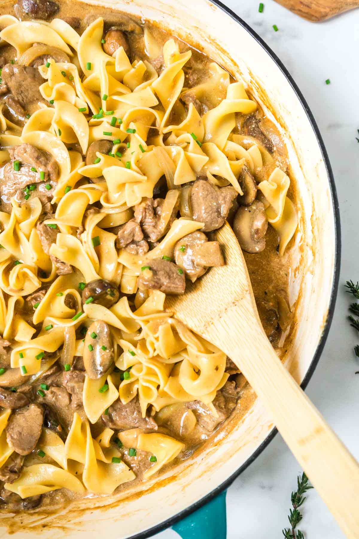 Beef stroganoff with egg noodles in a pan with a wooden spoon.