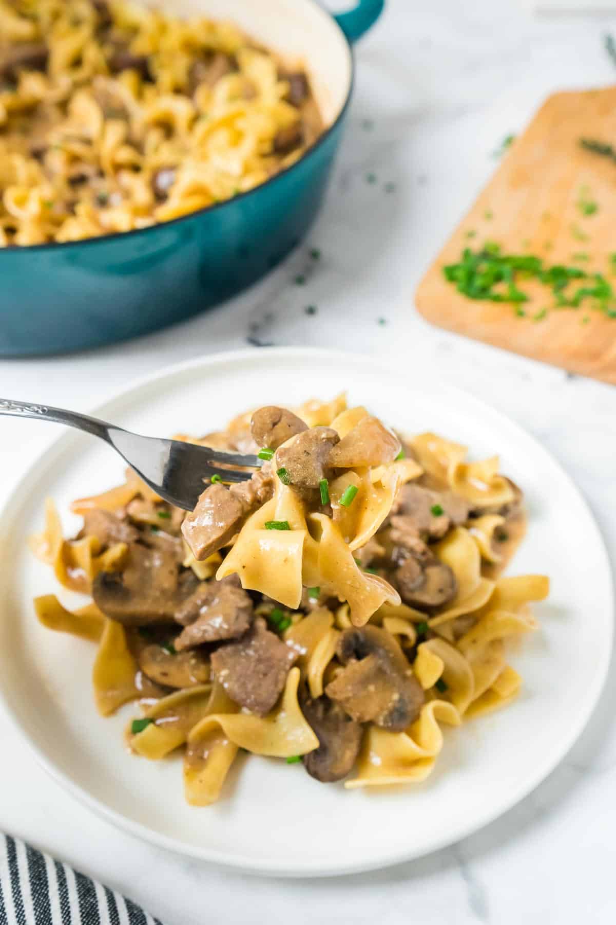 Beef stroganoff with egg noodles on a fork over a plate. 