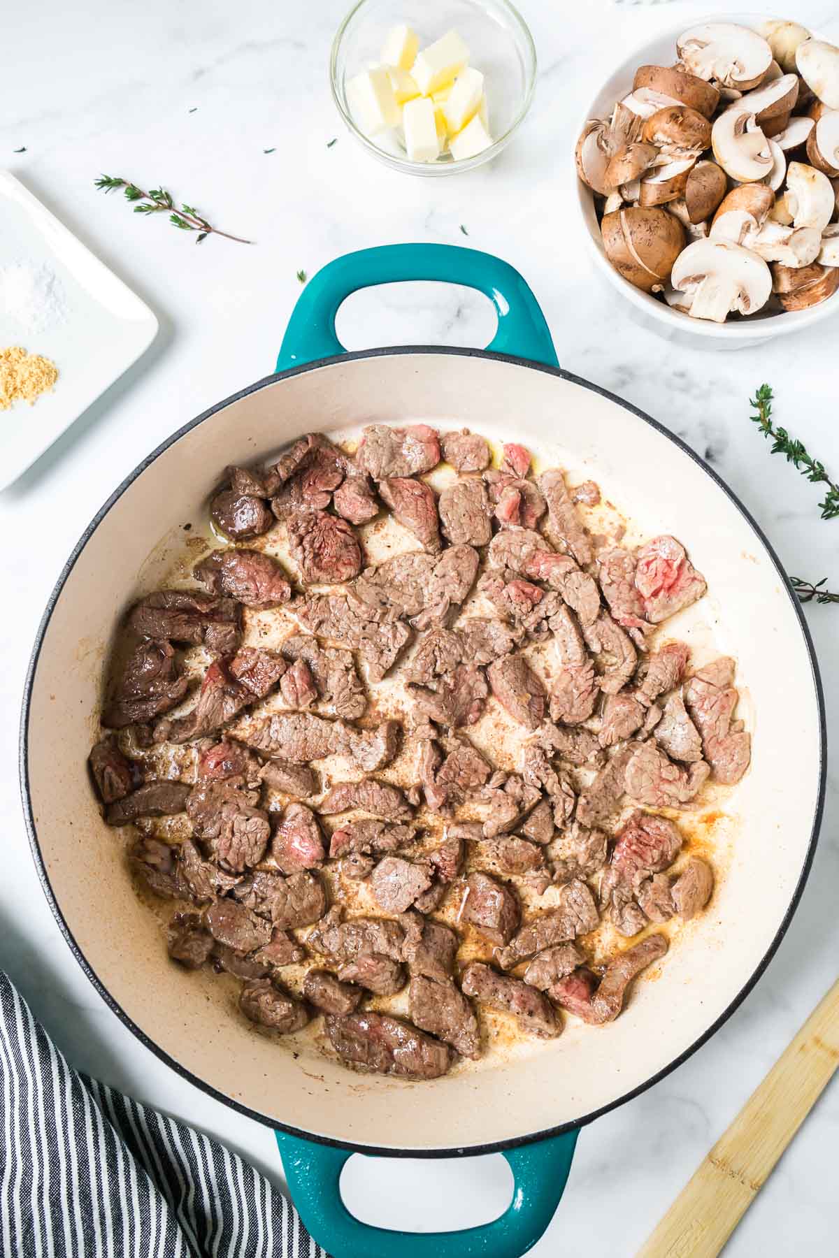 Tender beef in a pan cooking with a wooden spoon.