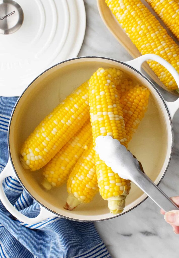 A large pot with 4 ears of cooked corn on the cob.