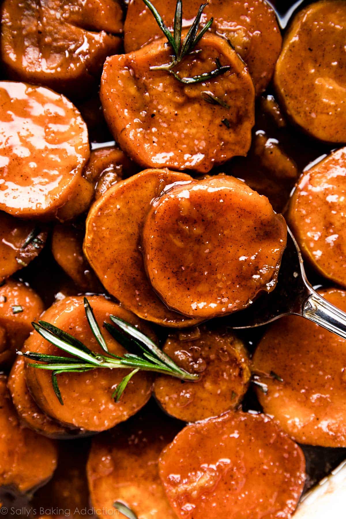 A pan of candied sweet potatoes garnished with rosemary.
