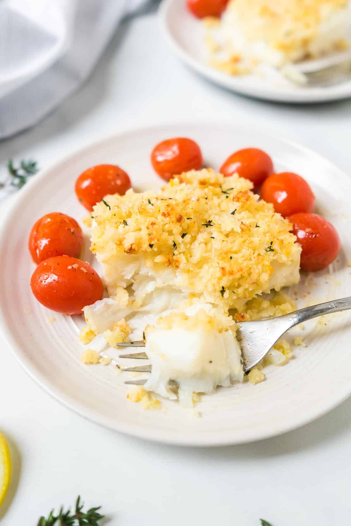 Cod with panko and parmesan crust on a plate with cherry tomatoes and a fork. 