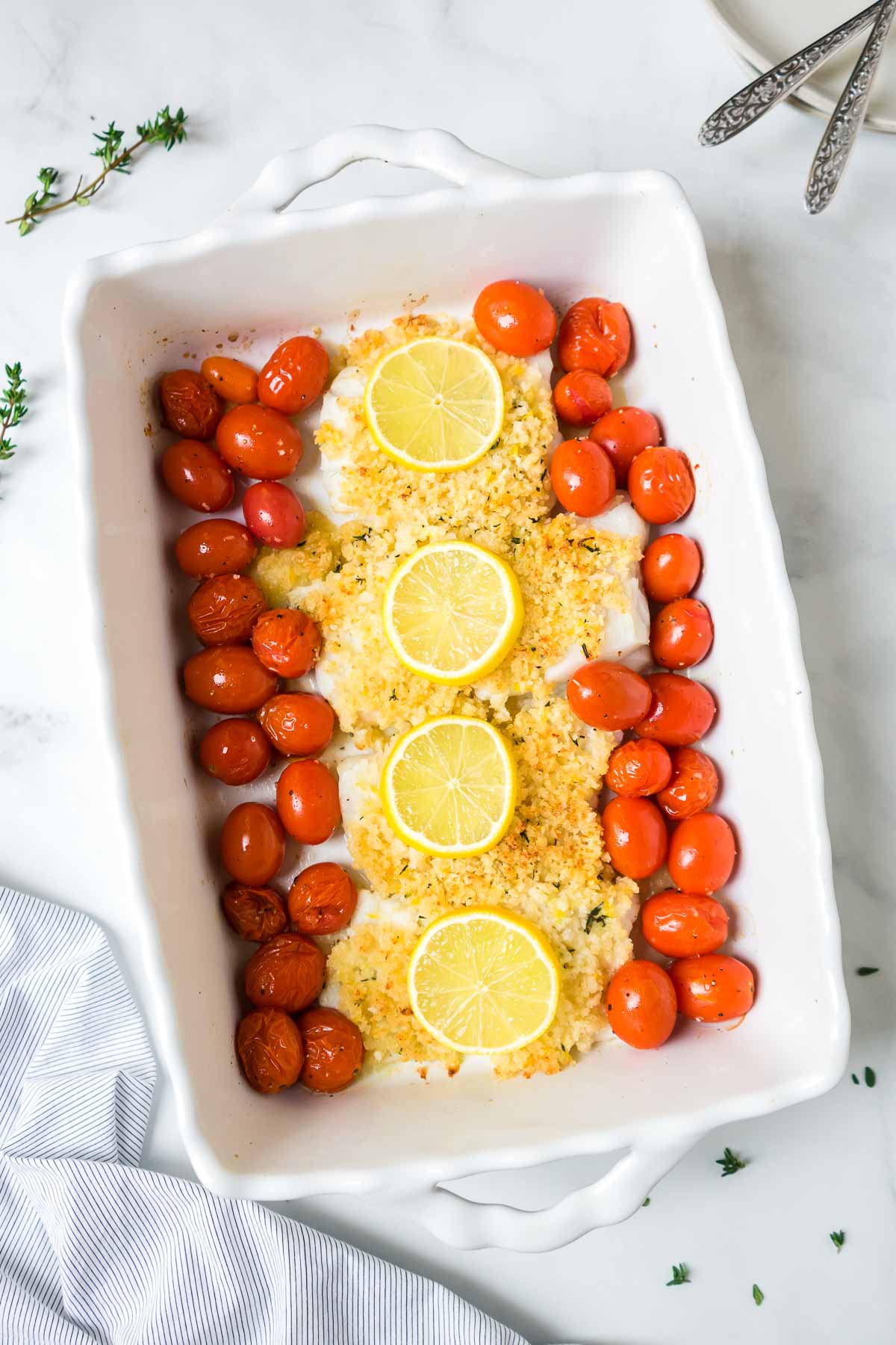 Panko and parmesan crusted cod in a large white baking dish with cherry tomatoes. 