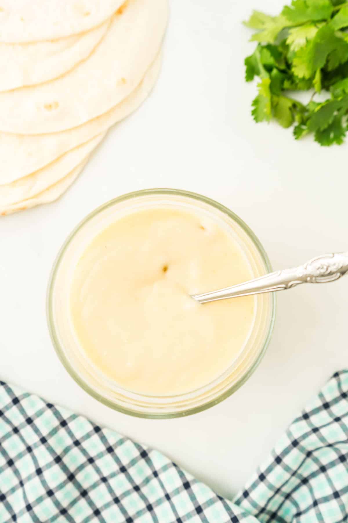 Sour cream enchilada sauce in a jar with cilantro around it. 
