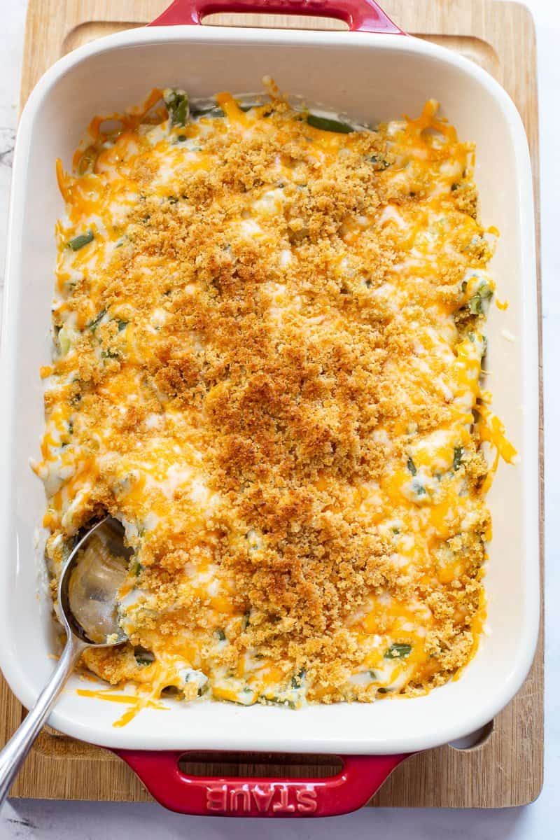 A large red baking ban with homemade green bean casserole topped with cheese and breadcrumbs.