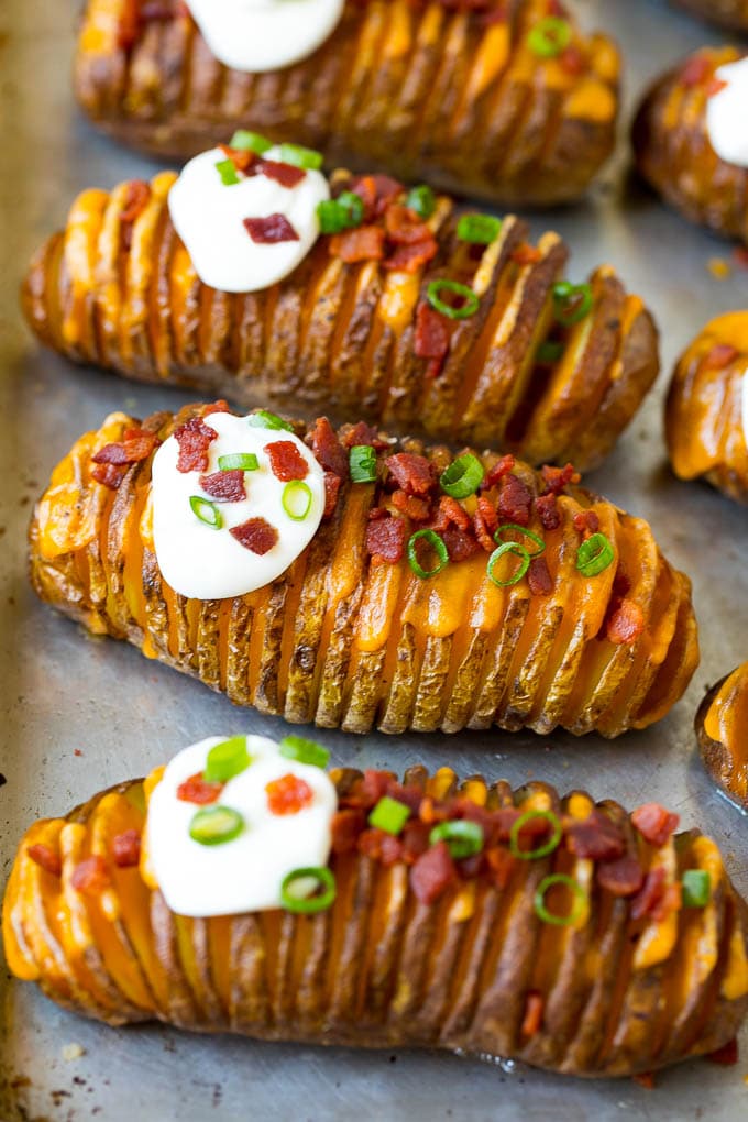 Hasselback potatoes on a baking sheet with bacon and sour cream.