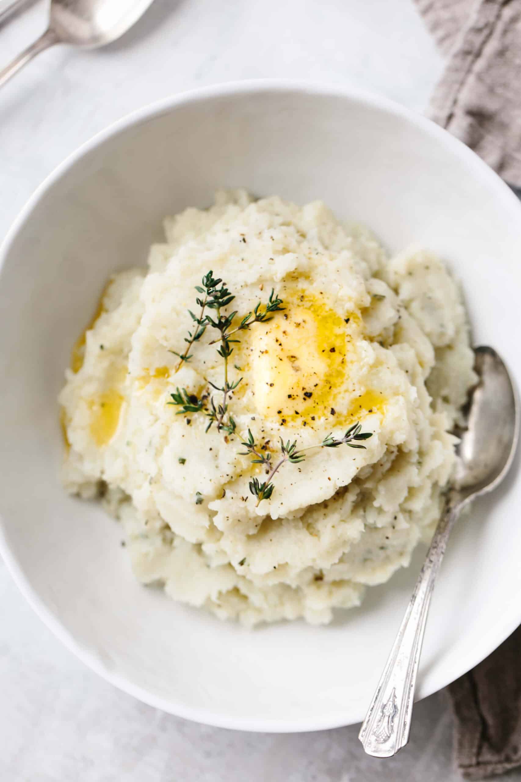 Cauliflower mashed potatoes in a bowl with butter and fresh thyme.