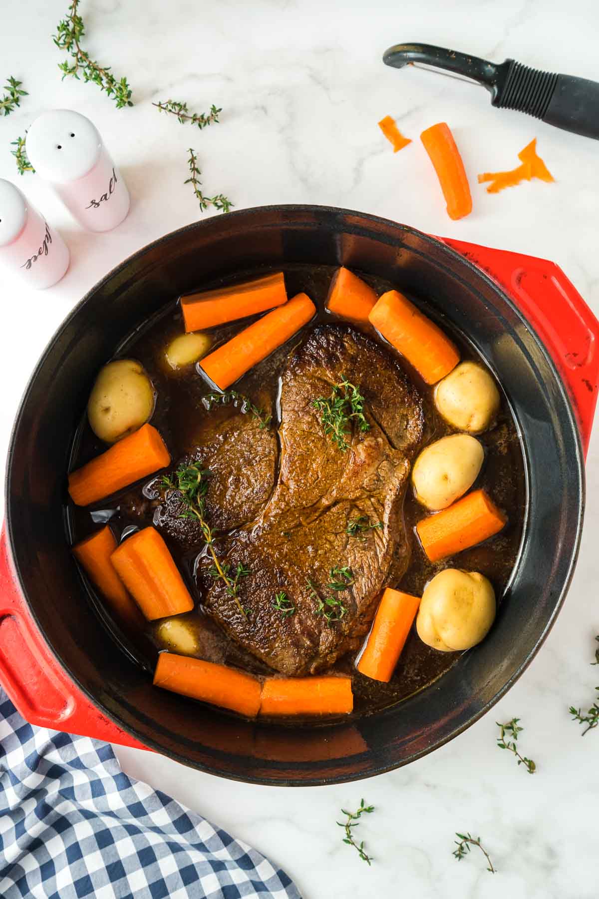 Pot roast in a dutch oven with carrots and potatoes before cooking in the oven.
