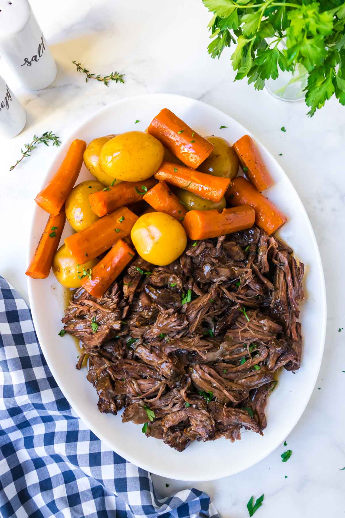 A large white plate of pot roast with veggies with a blue and white linen.