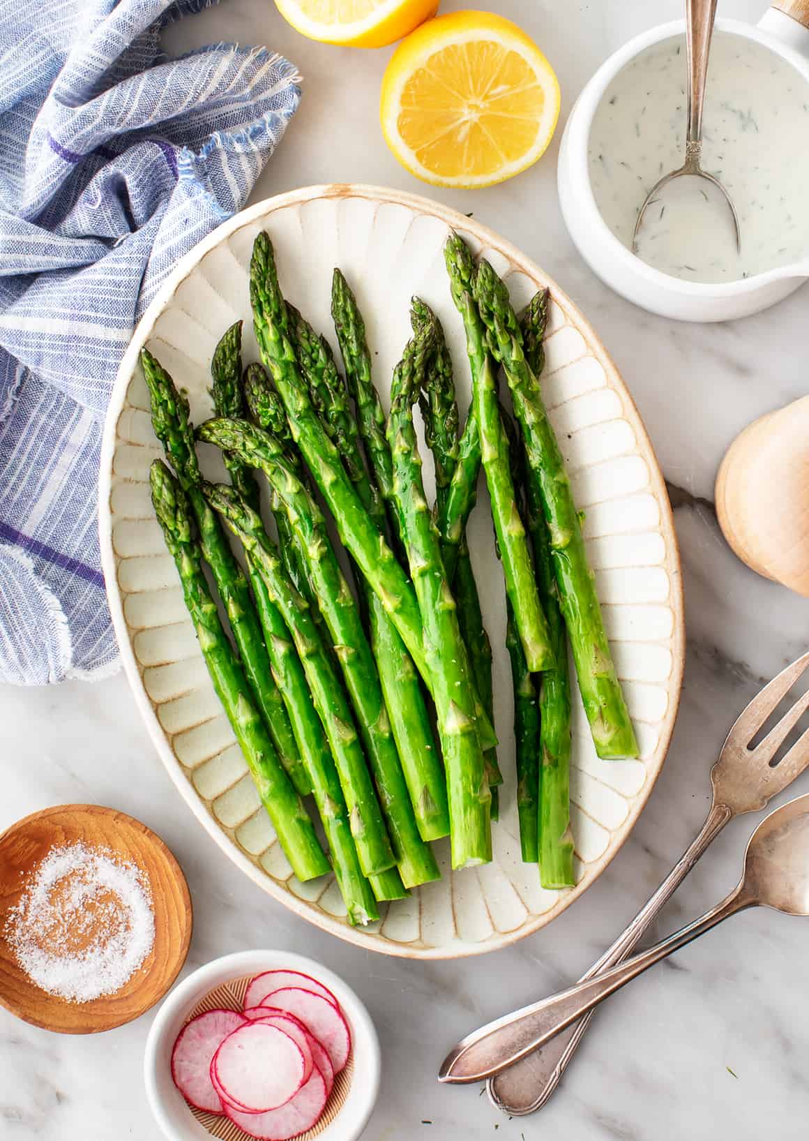 Roasted asparagus on a plate with spices and a sauce on the side.