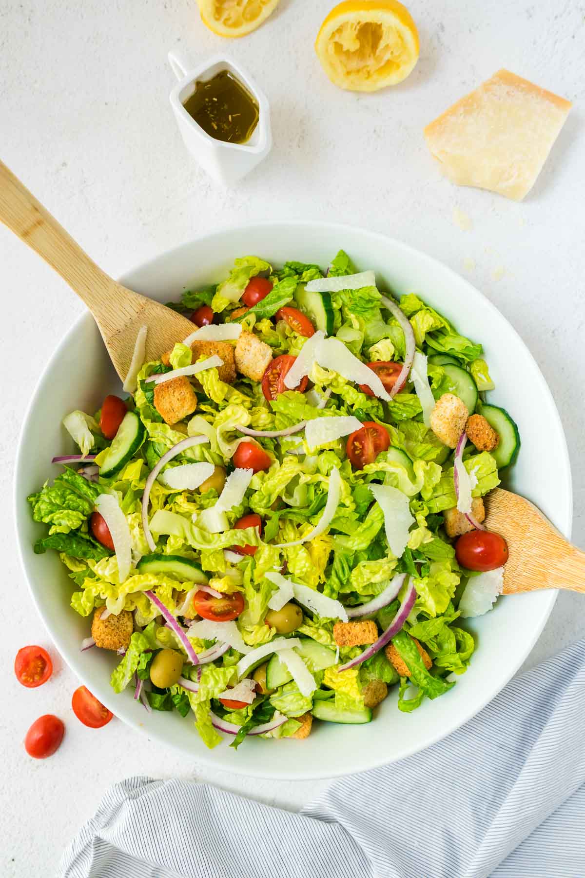 Large tossed green salad in a white serving bowl with two wooden serving spoons.