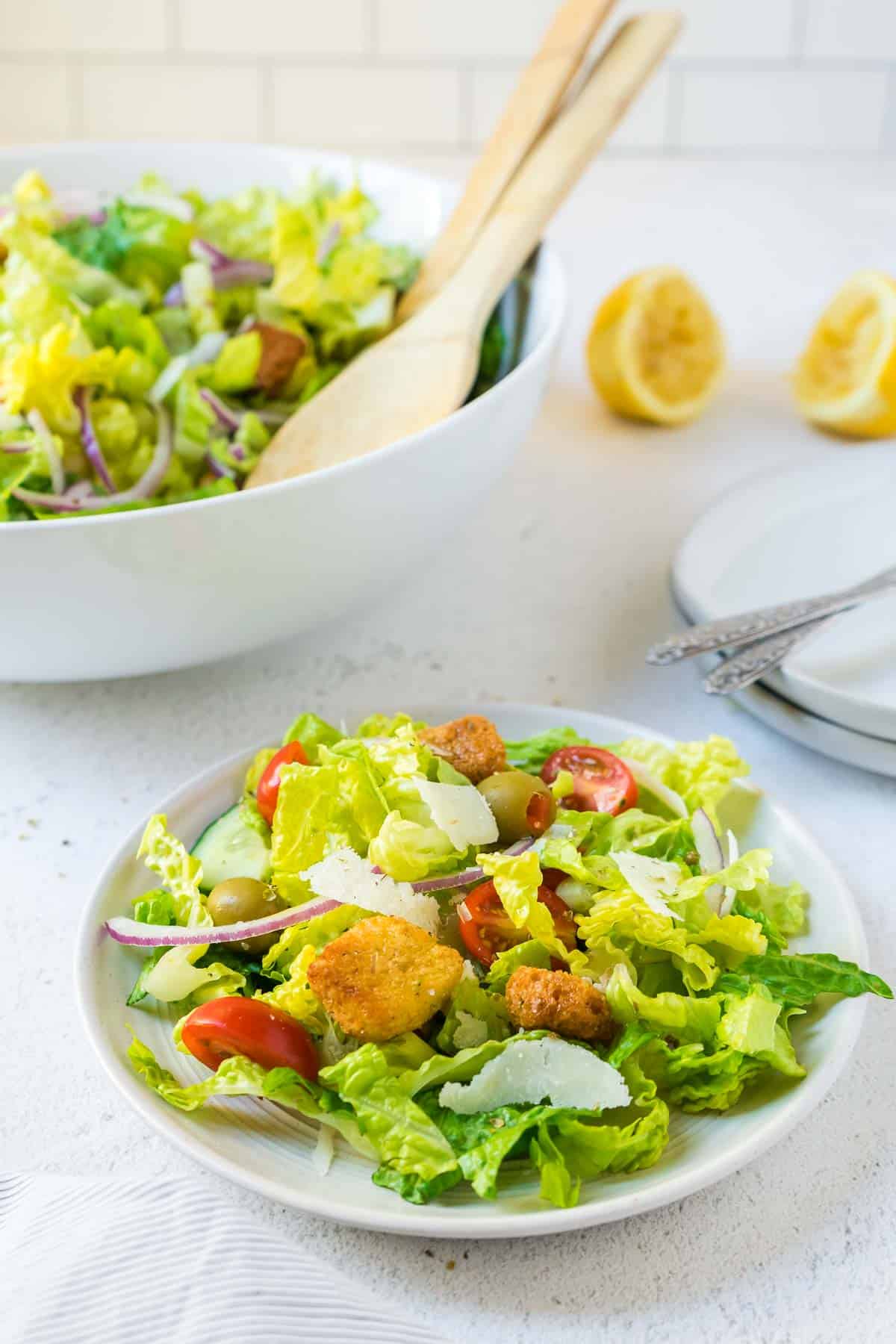 Simple tossed green salad on a small salad plate with the larger salad bowl in the background. 