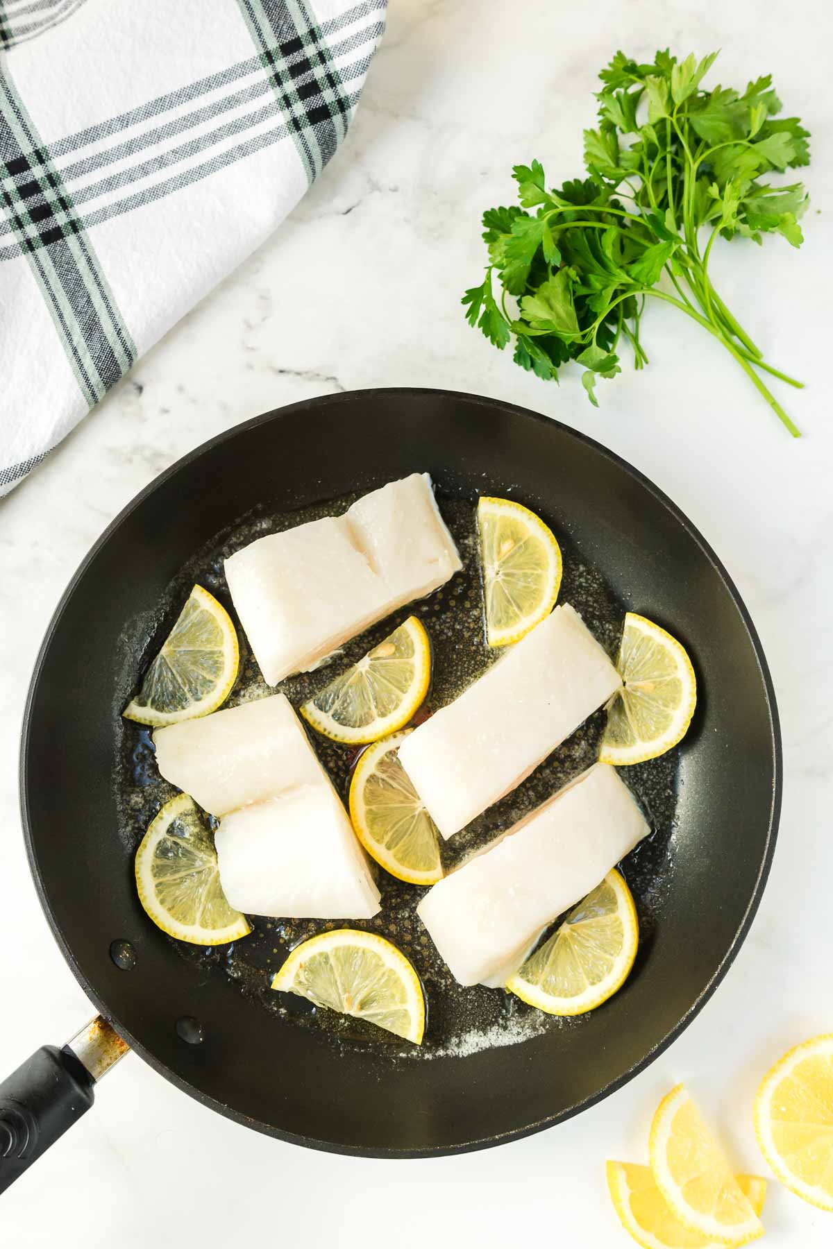 Raw Chilean sea bass in a pan with lemons.