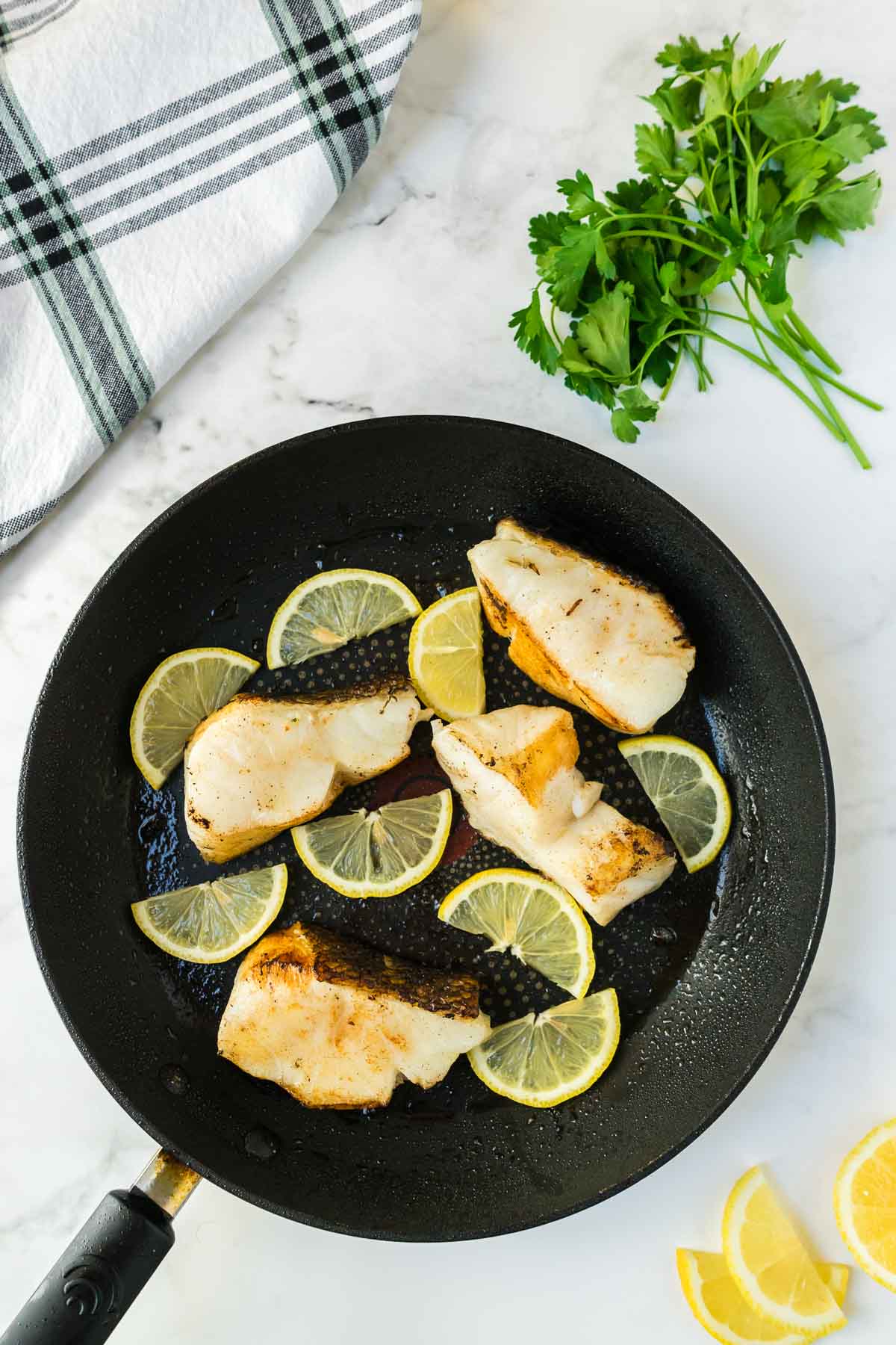 Chilean sea bass cooking in a pan with lemons.