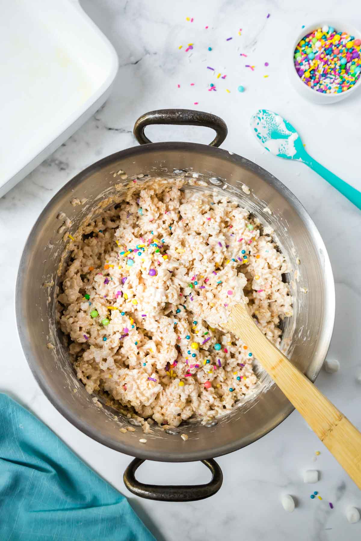 A large pan with a wooden spoon stirring the rice krispies treats.