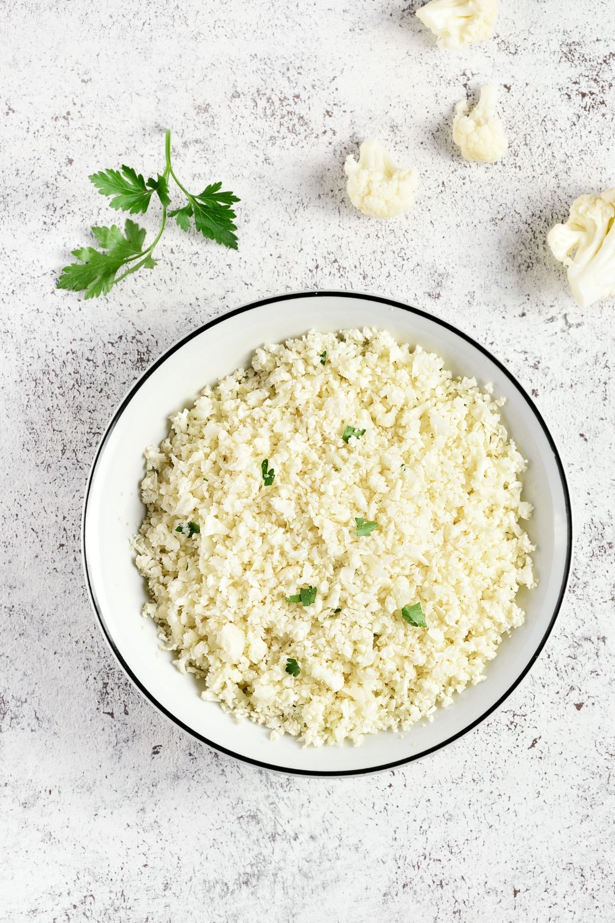 cauliflower rice in a white bowl sprinkled with parsley.