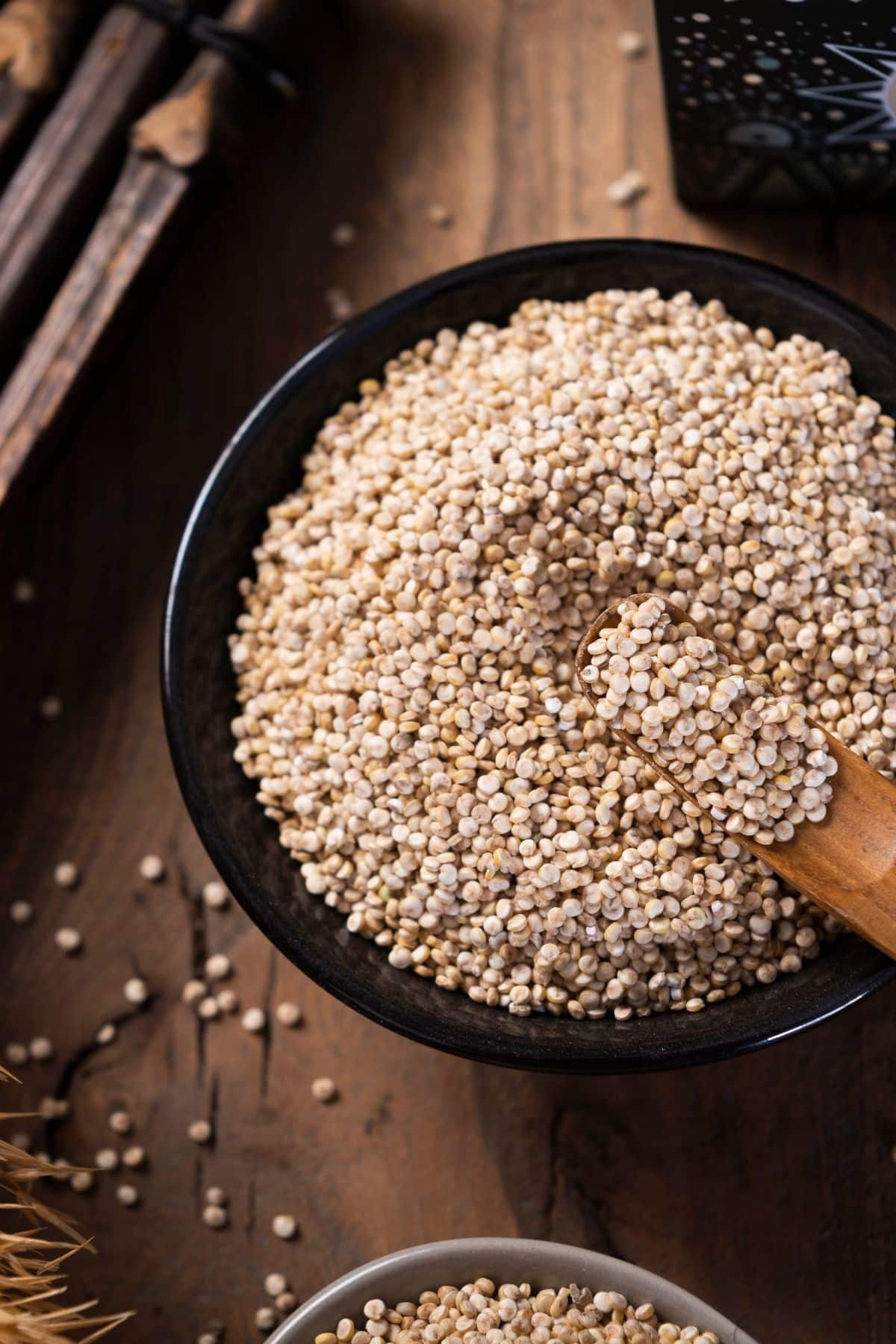 Dried quinoa in a black bowl with a wooden spoons.