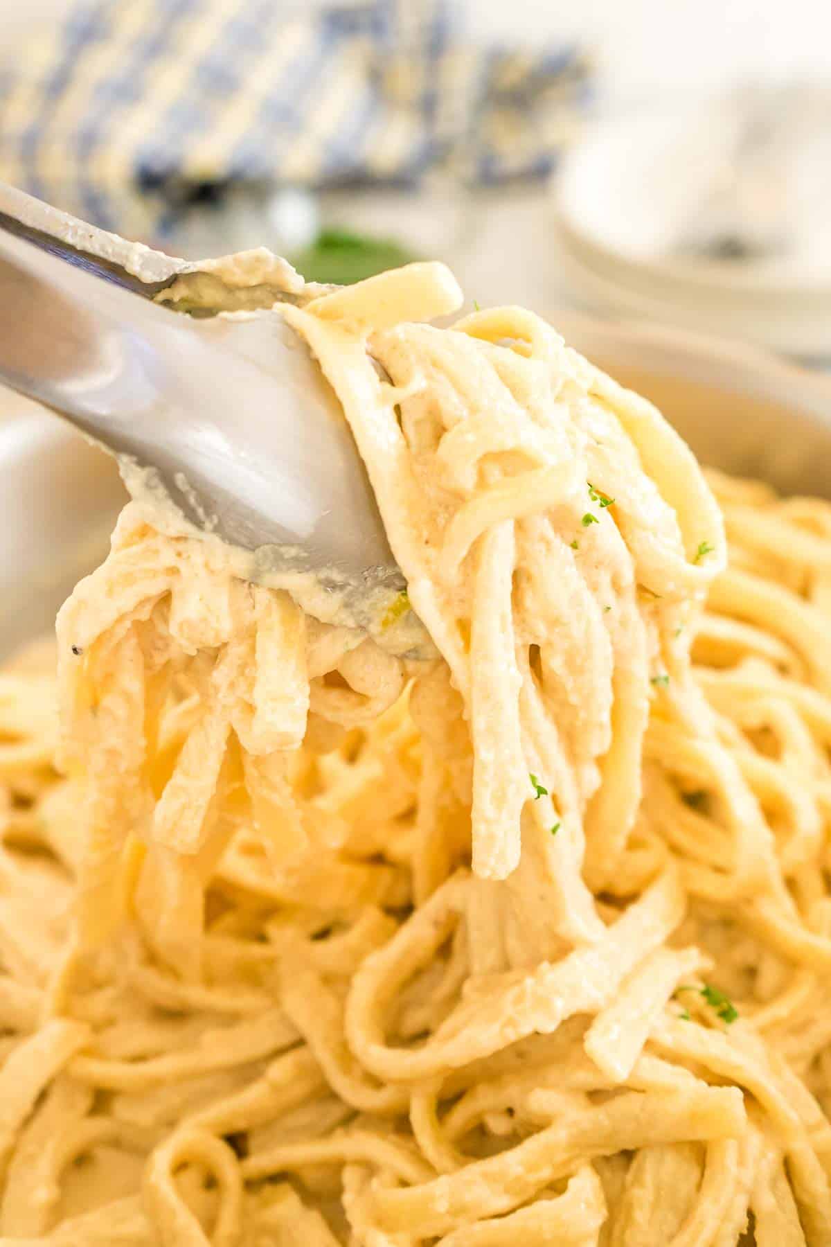 Close up of tongs scooping up tahini pasta.