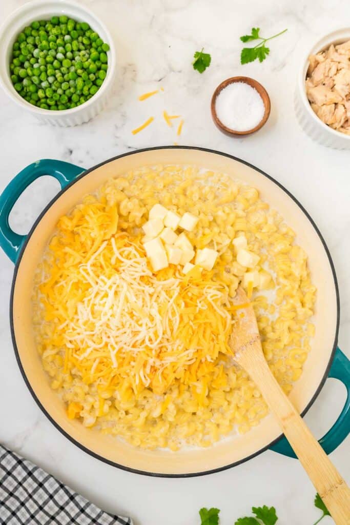 Macaroni in a pan with cheese and butter being added.