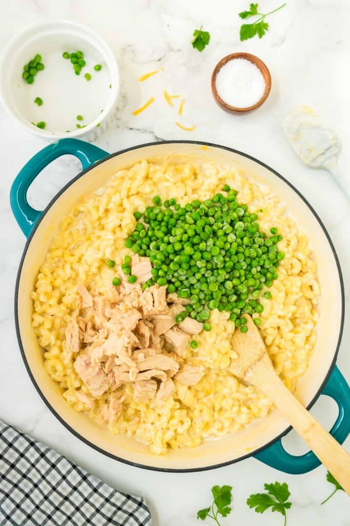 Macaroni cooking in a pan and tuna and peas being added.