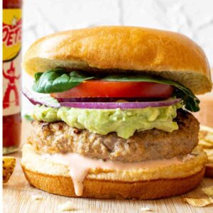 A spicy turkey burger with lettuce, tomato, onion, and secret sauce dripping on a bun.