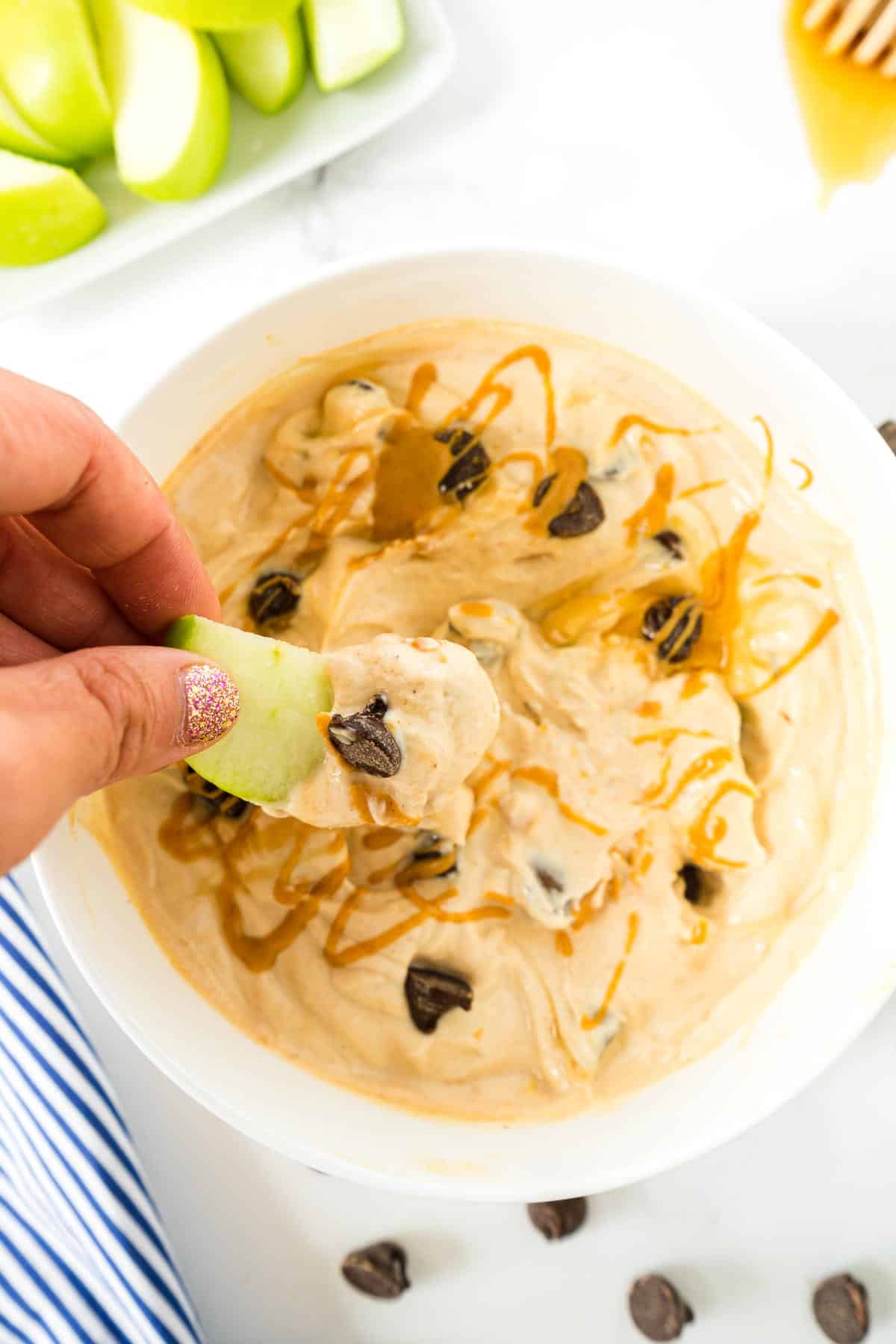 A green apple being dipped in this Cookie Dough Greek Yogurt.