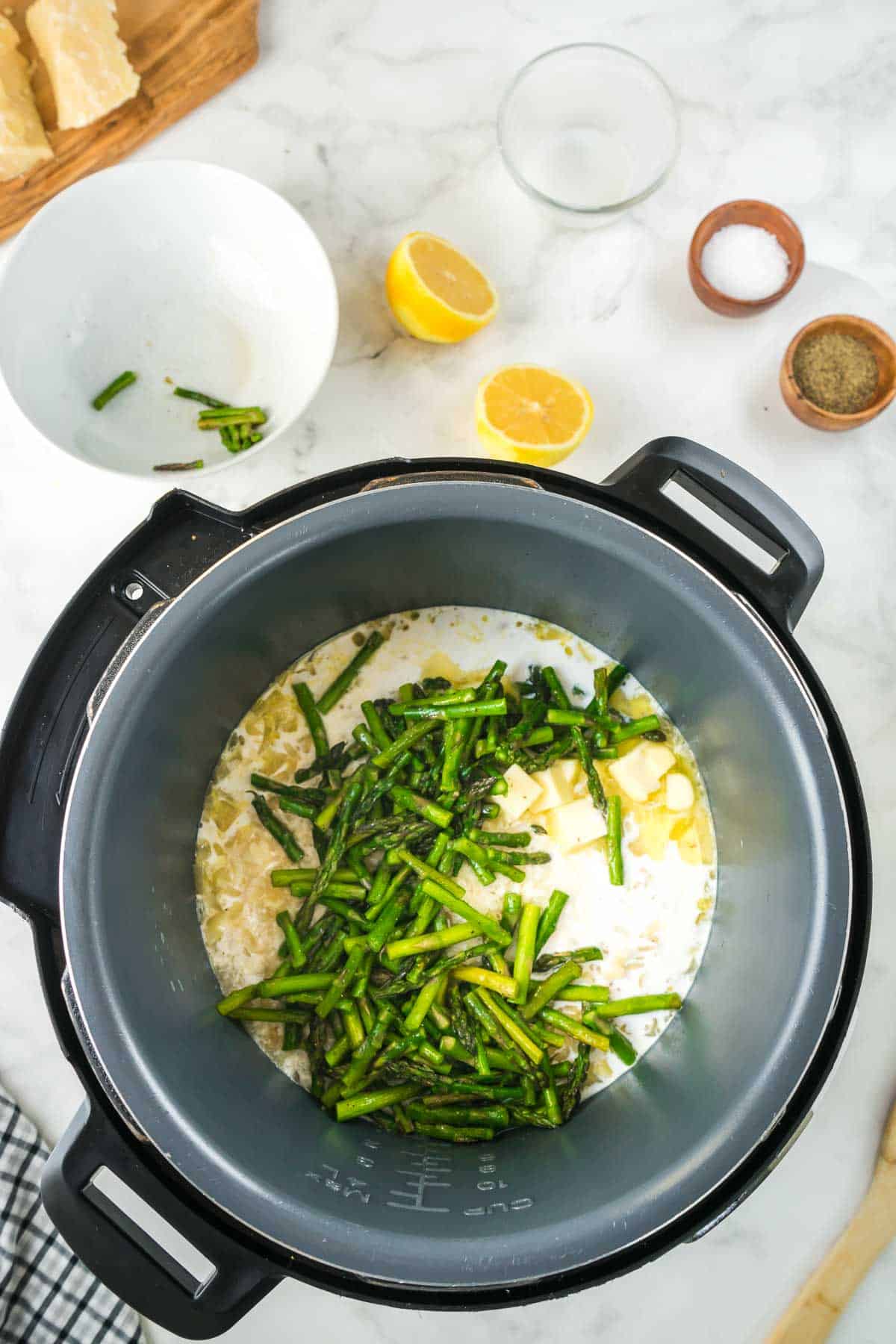 Asparagus and additional ingredients being added to the instant pot with the arborio rice.