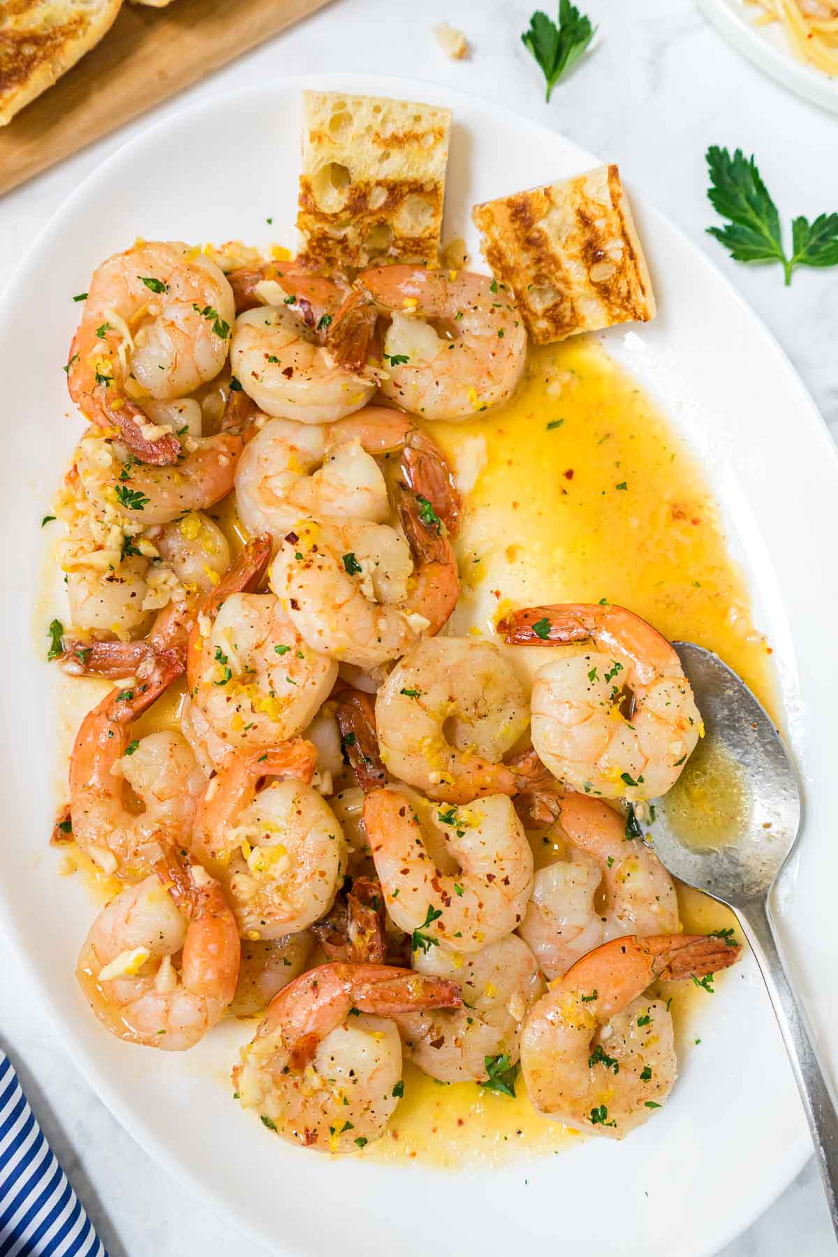 Easy Shrimp Scampi Recipe Without Wine on a white serving platter with garlic bread and a spoon.