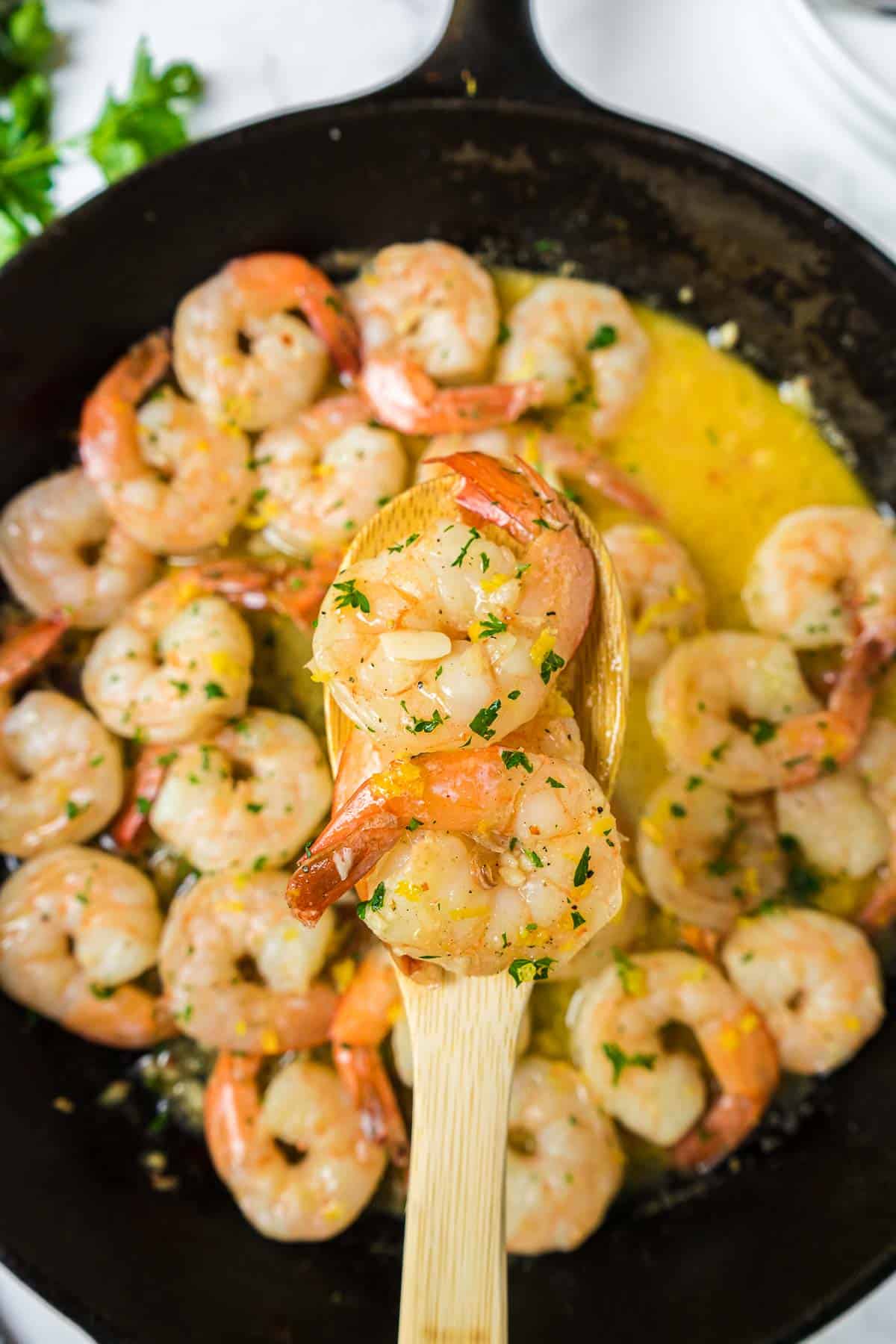 Close up of garlic butter shrimp on a wooden spoon.