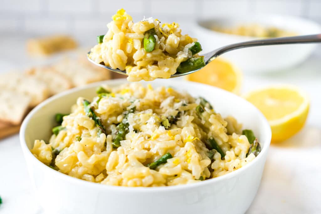 A bowl of instant pot risotto with asparagus in a white bowl with a spoon of it above the bowl.