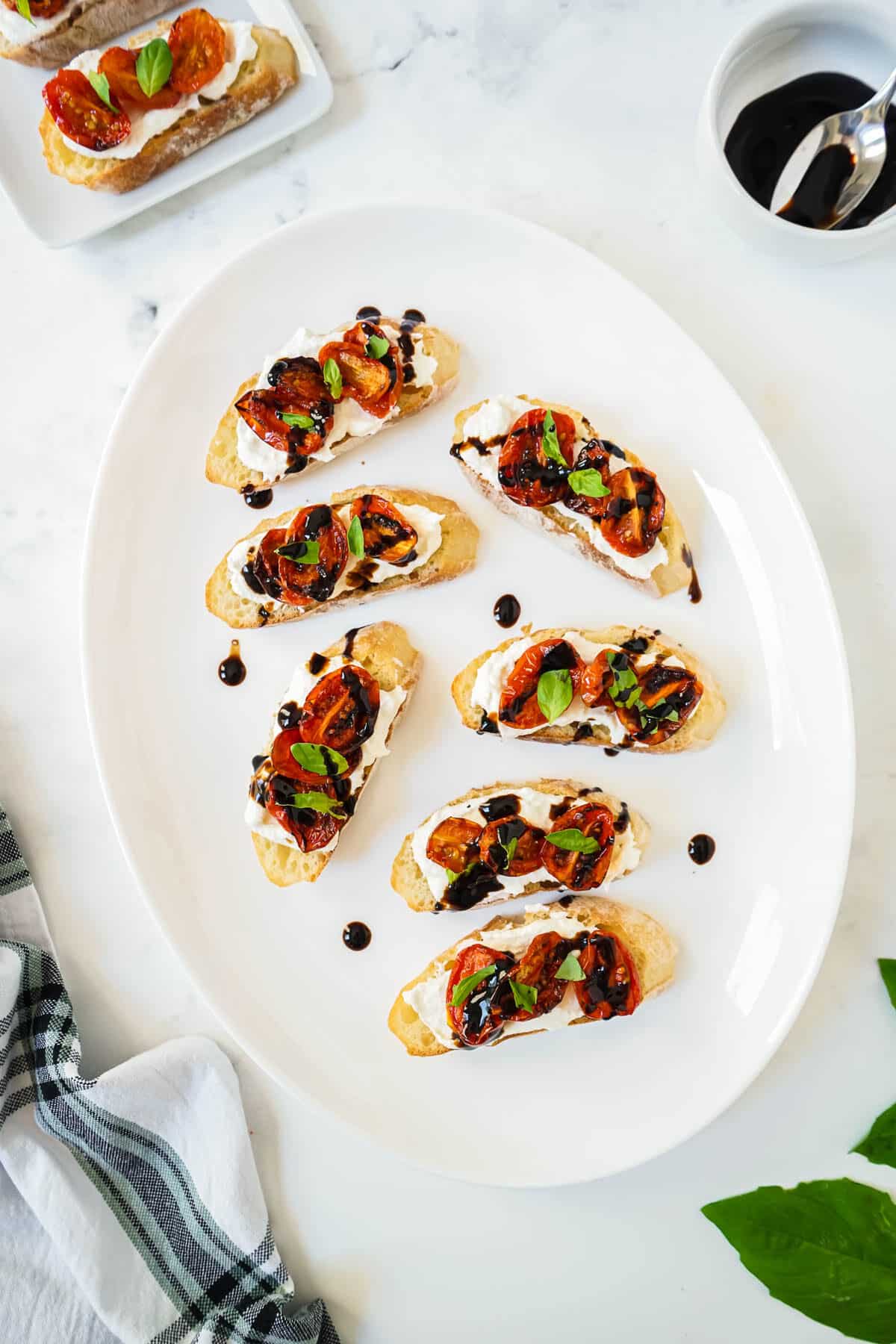 Roasted tomato bruschetta on a white plate drizzled with balsamic glaze.