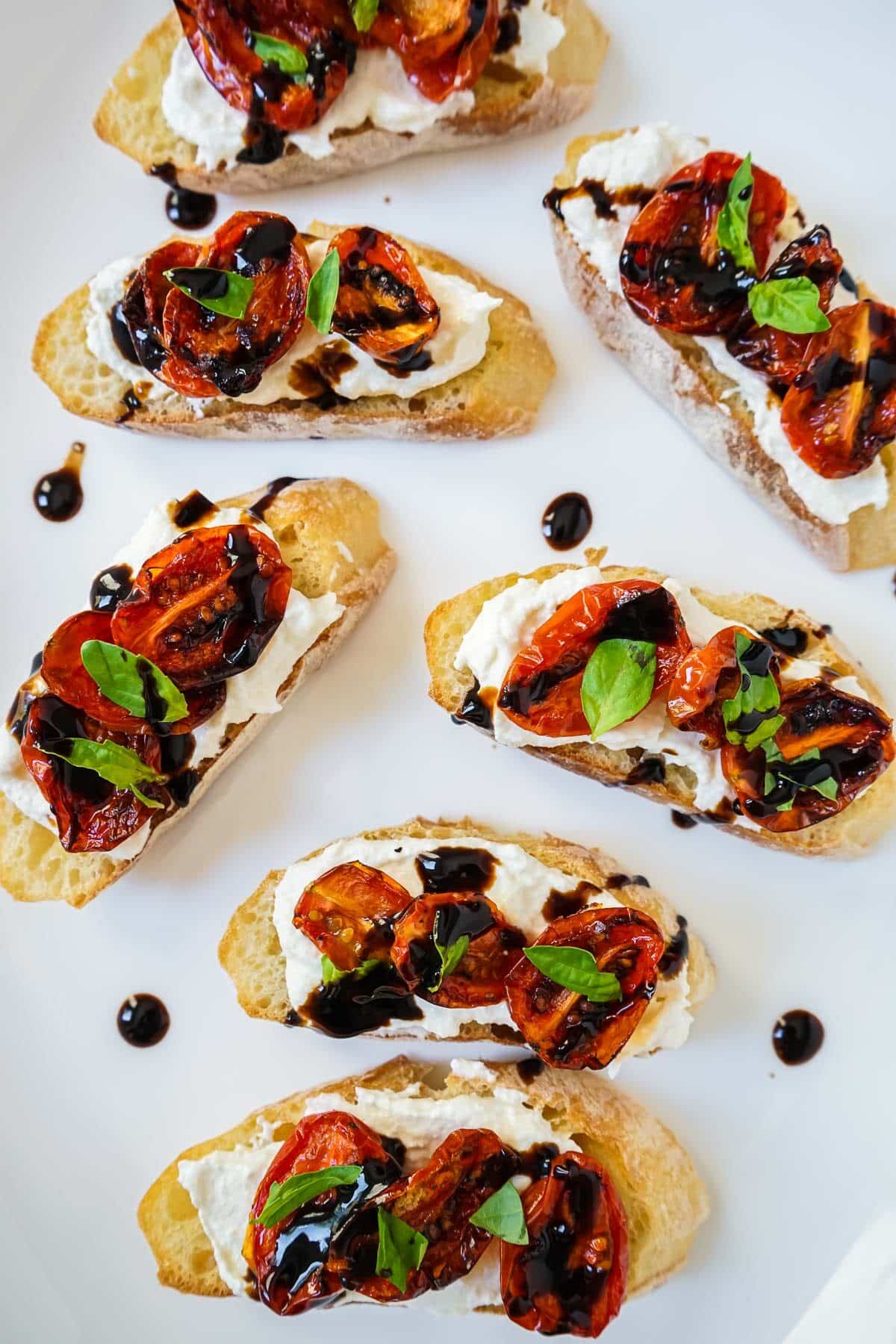 Roasted tomato bruschetta on a white plate drizzled with balsamic glaze.