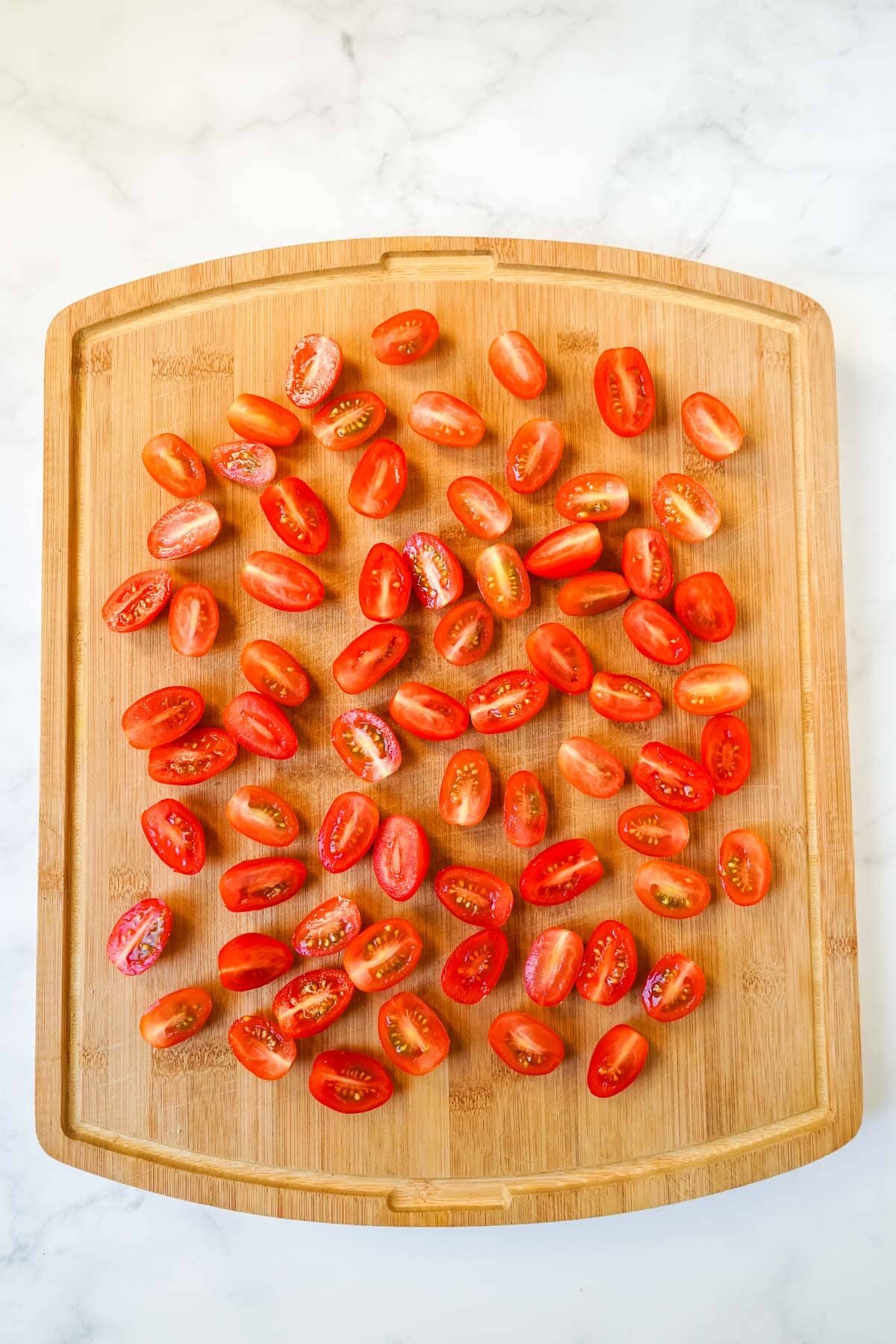 A bunch of cherry tomatoes cut in half on a cutting board.