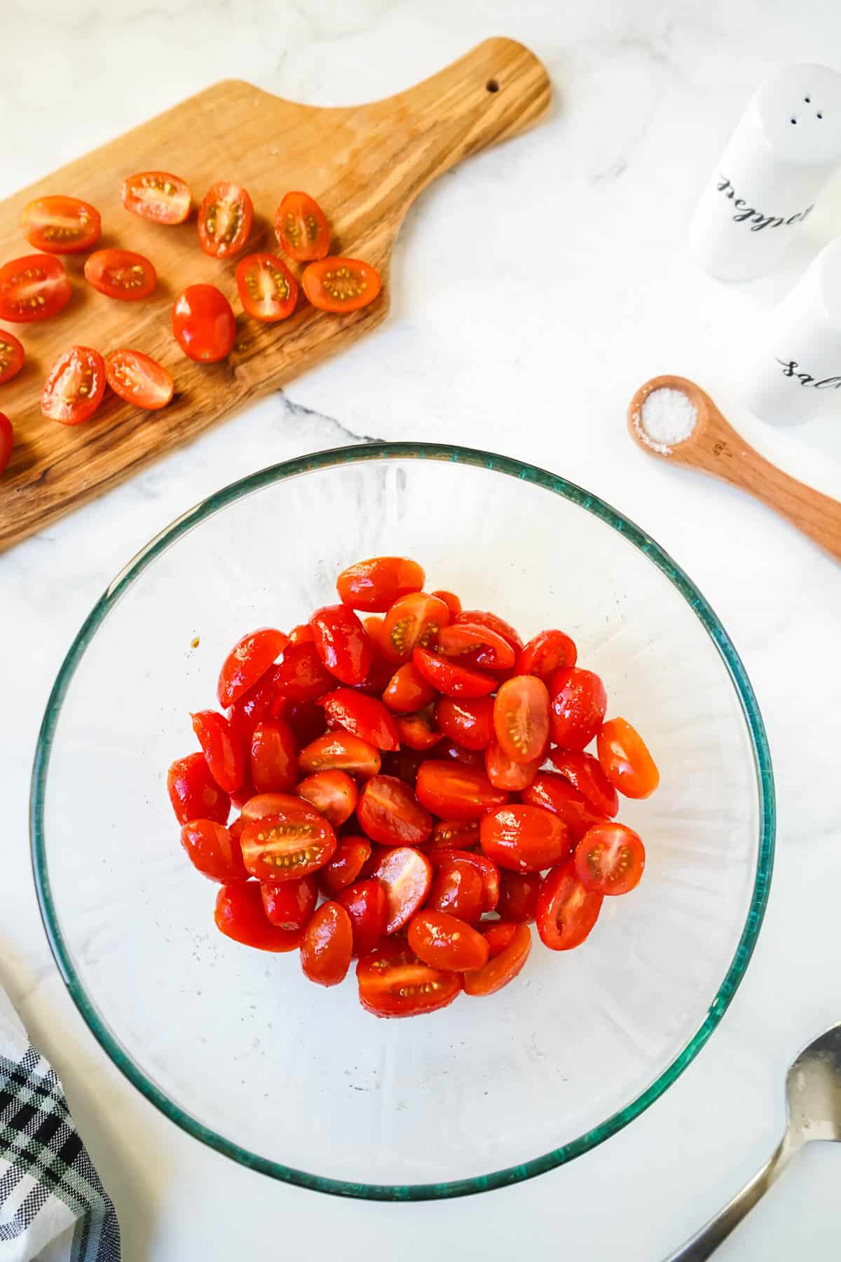 Cherry tomatoes in a glass bowl tossed with olive oil, sugar and salt.