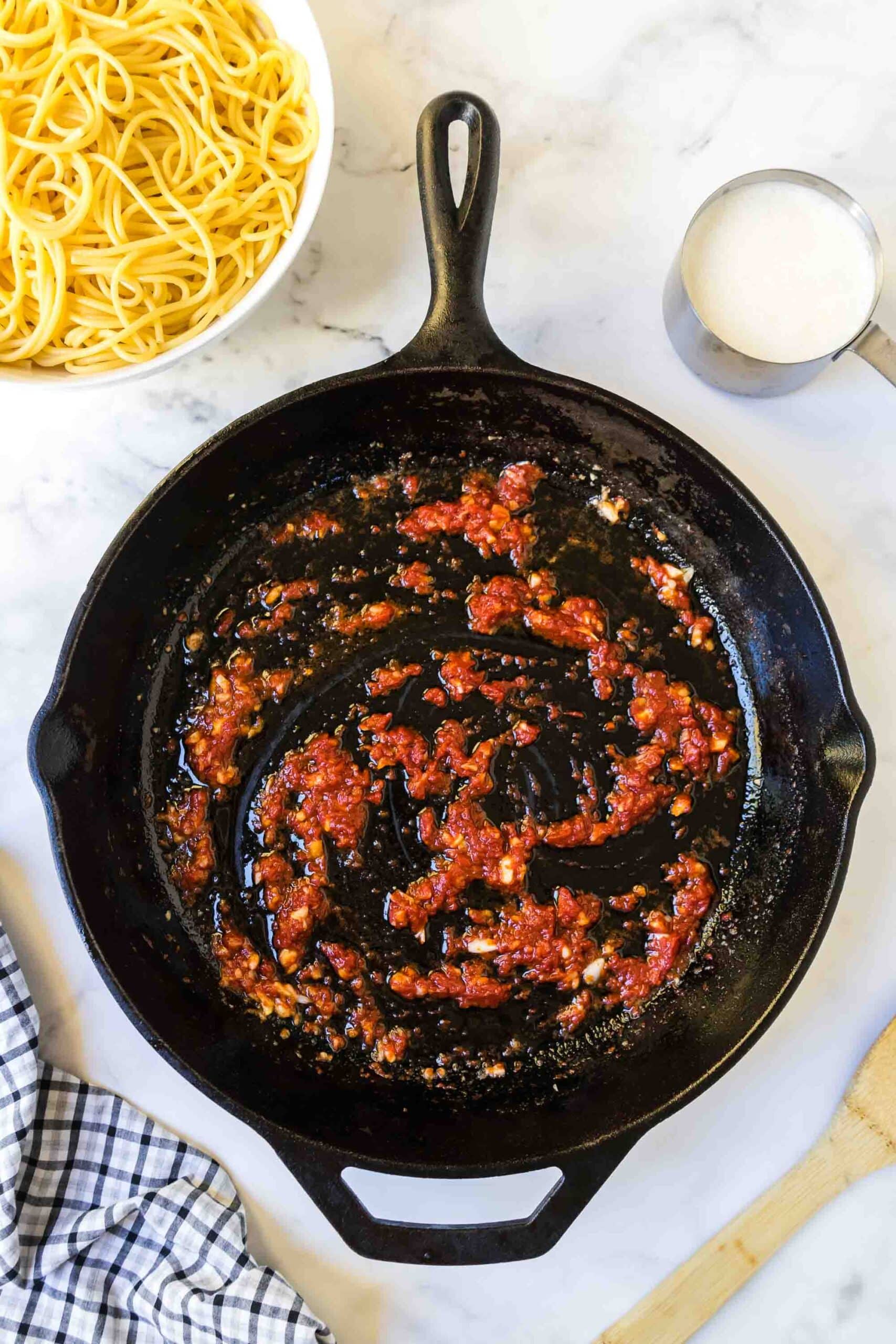 Tomato paste and garlic being cooked in an iron skillet.