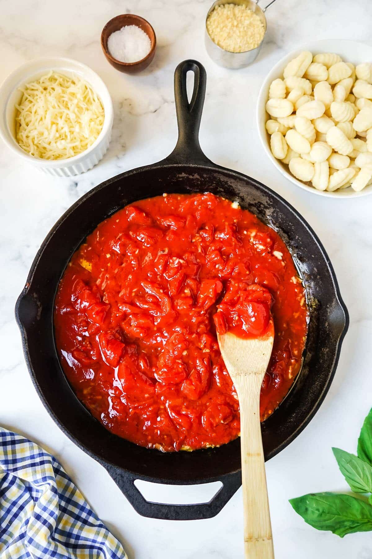 San Marzano tomatoes being added to the skillet with a wooden spoon.