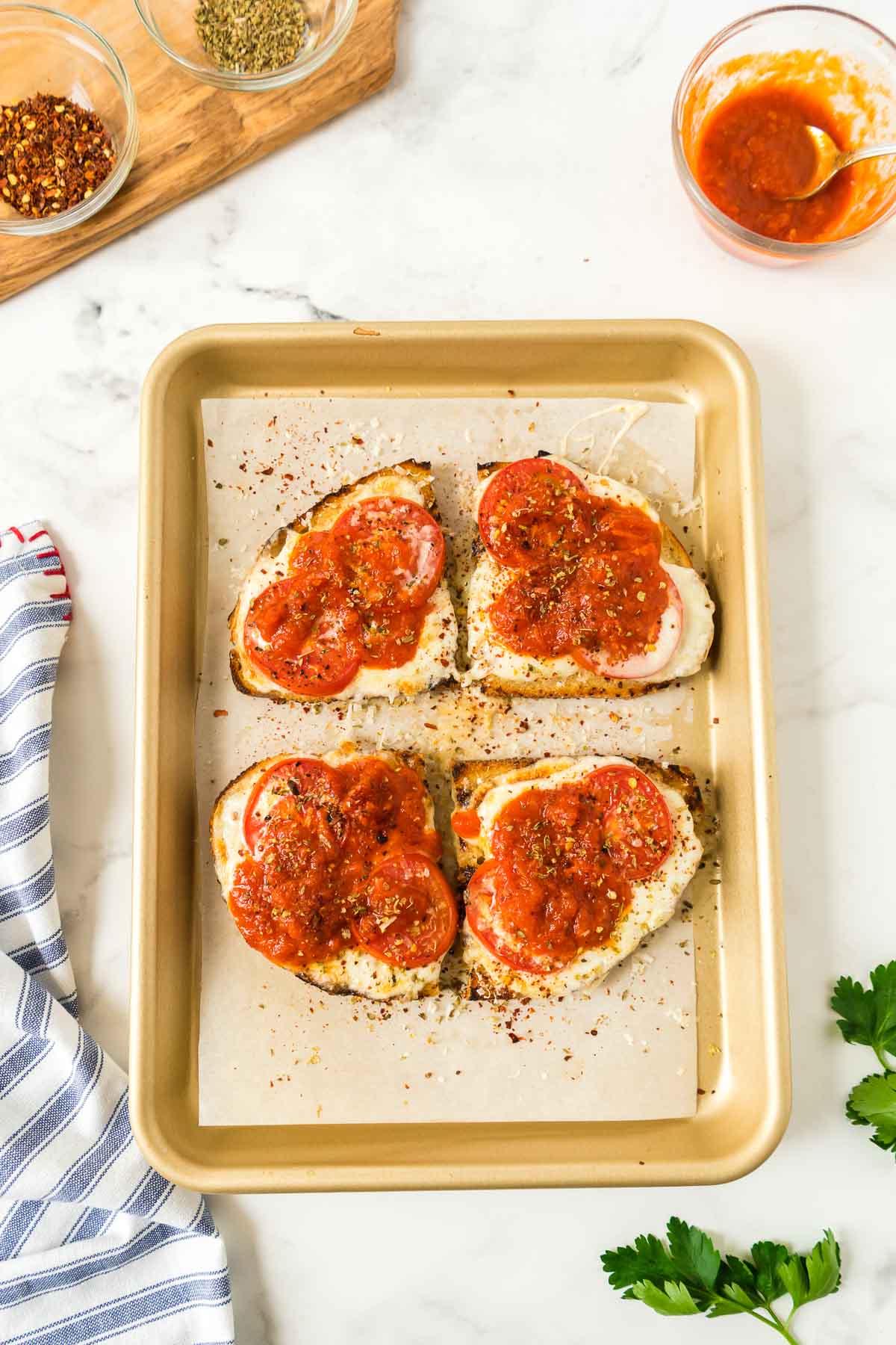 The finished viral pizza toast recipe (Hailey Bieber) with warm marinara, red pepper flakes, oregano and Parmesan cheese on a small baking sheet.