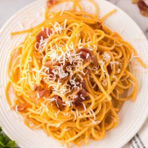 Creamy spaghetti with bacon on a white plate garnished with parmesan cheese.