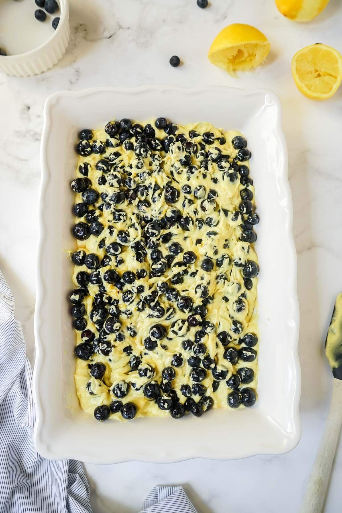 Blueberries being added to the batter in a white baking dish.