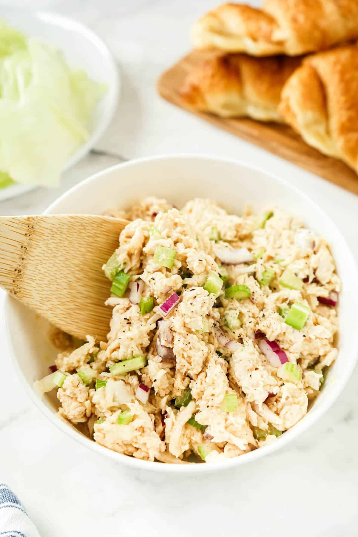 Chicken salad made without mayo in a white bowl with a wooden spoon.
