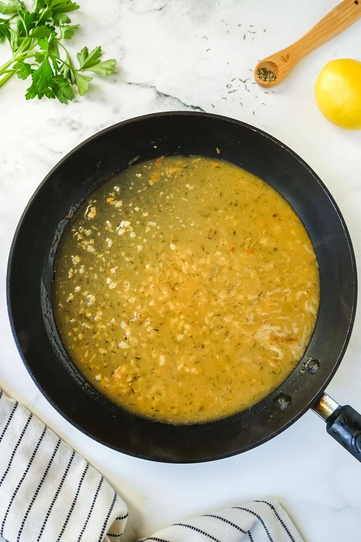 The lemon and white wine sauce cooking in a pan.