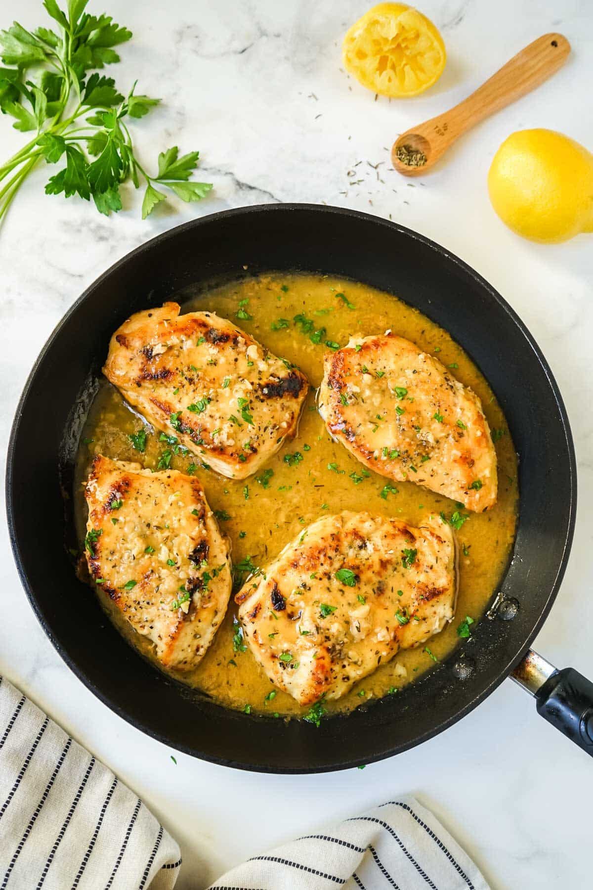 Chicken in white wine sauce in a black pan.