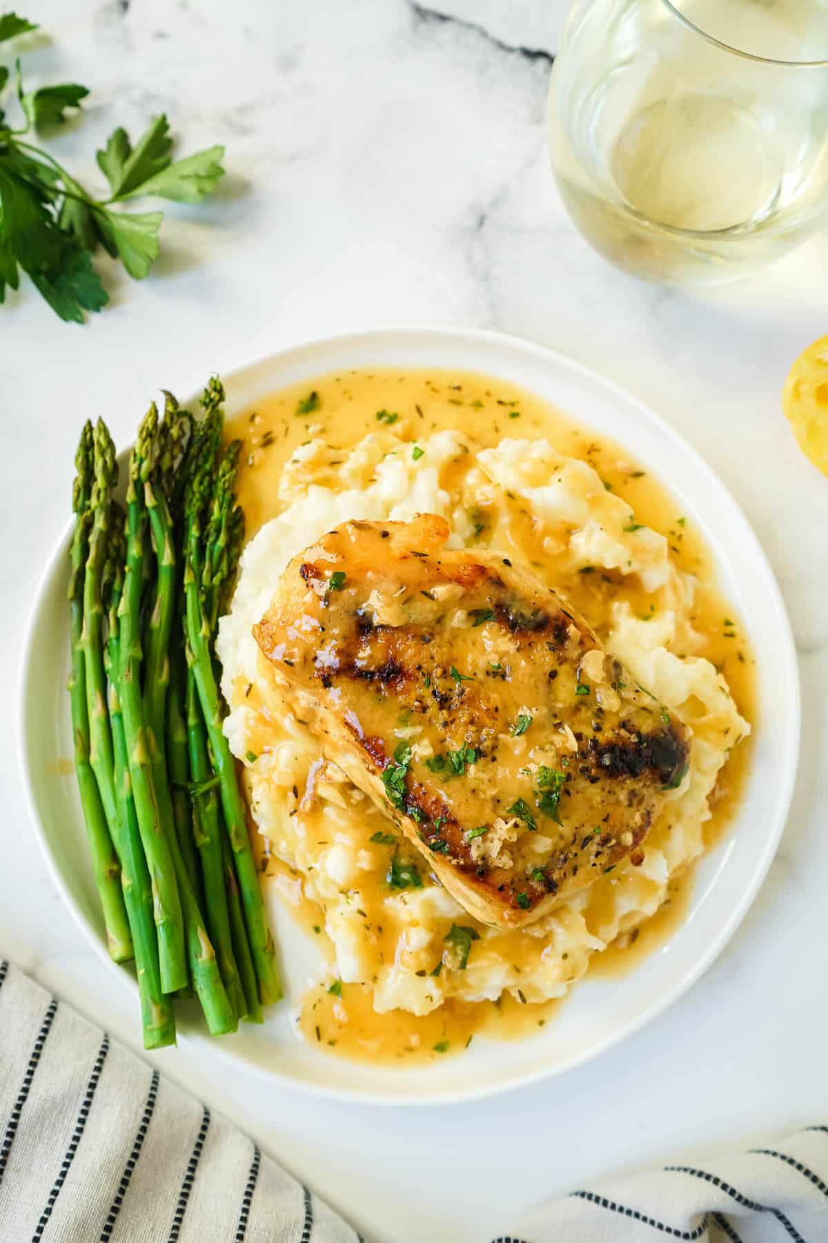 Chicken with white wine sauce without cream on a white plate with mashed potatoes and asparagus.
