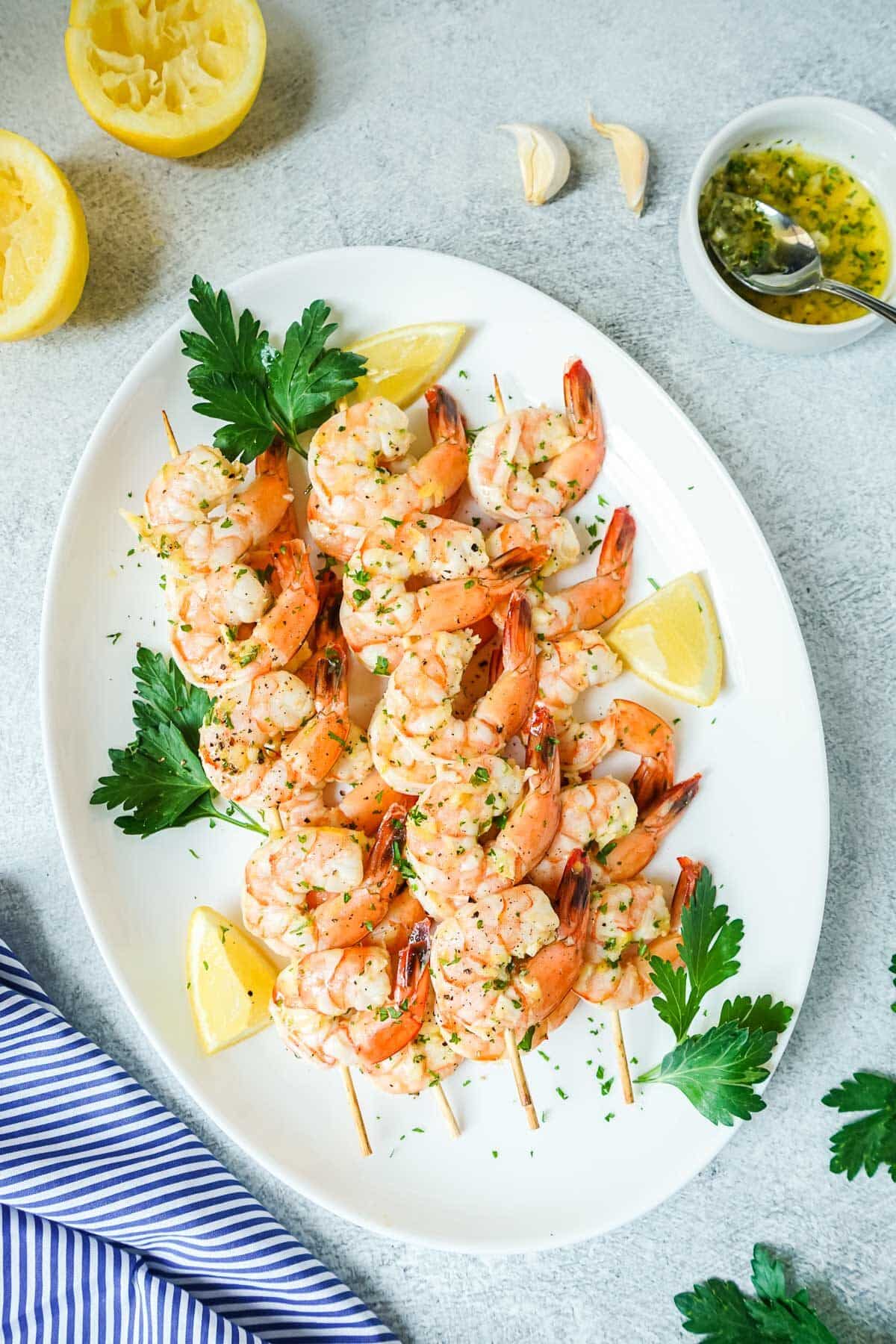 Oven baked shrimp skewers on a large white platter with lemon and parsley.