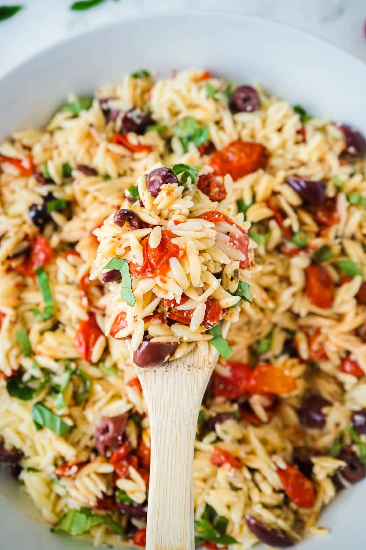 Close up of pasta salad with roasted tomatoes on a wooden spoon.