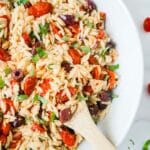 Pasta salad with roasted tomatoes in a white bowl with a wooden spoon.